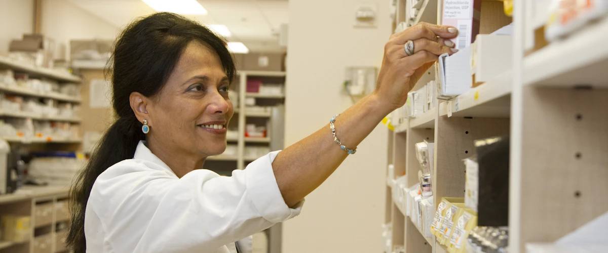 Farmacéutica examinando medicamentos en las estanterías de su lugar de trabajo