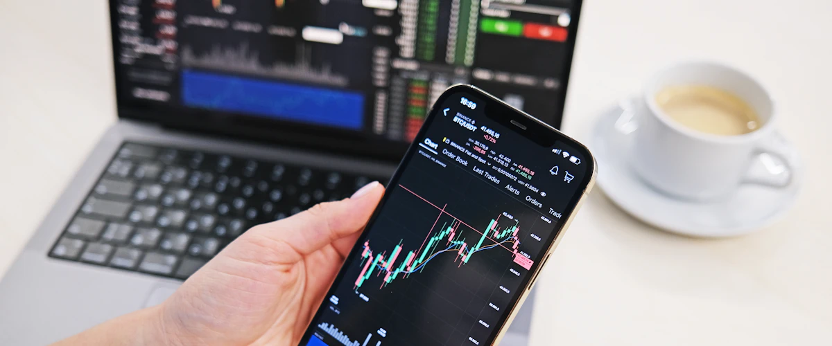 Mano consultando un teléfono frente a la pantalla de un ordenador