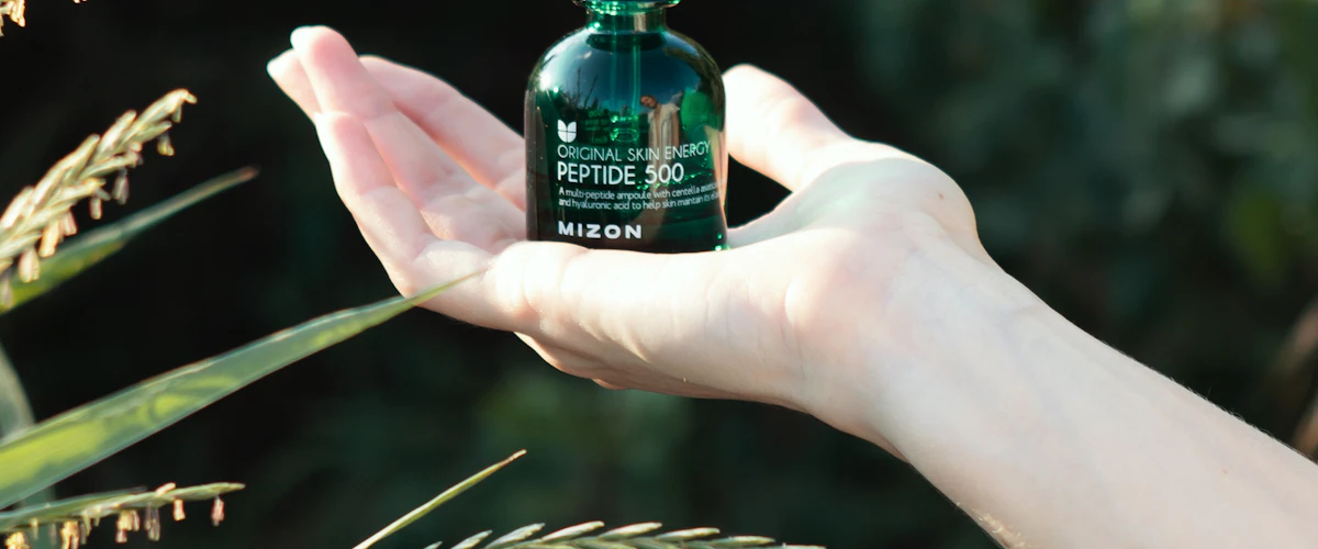 Mano sostiene un pequeño frasco de aceite cosmético sobre un fondo neutro