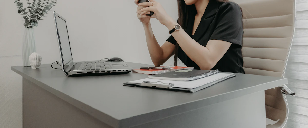 Profesional revisa mensajes en su teléfono móvil junto al portátil del escritorio