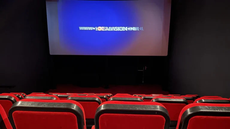 Sala de cine con butacas rojas frente a una pantalla de proyección