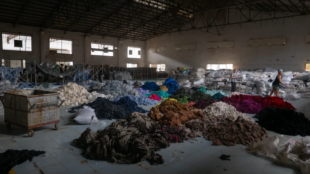 Trabajadores clasifican montones de ropa usada para reciclaje textil en una nave industrial